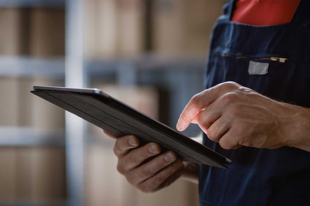 Ein Mann in Arbeitskleidung hält ein Tablet und betrachtet den Bildschirm aufmerksam