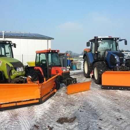 Drei Traktoren mit Schneepflügen, die im Schnee geparkt sind, umgeben von einer winterlichen Landschaft