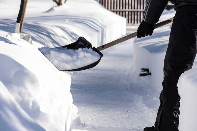 Eine Person schaufelt Schnee von einem Gehweg, um den Zugang zu erleichtern und die Sicherheit zu gewährleisten