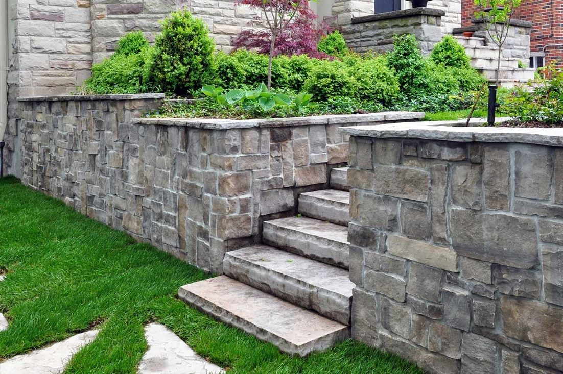 Stufen aus Stein führen an einer Mauer entlang zu einem Haus, umgeben von einer gepflegten Gartenlandschaft