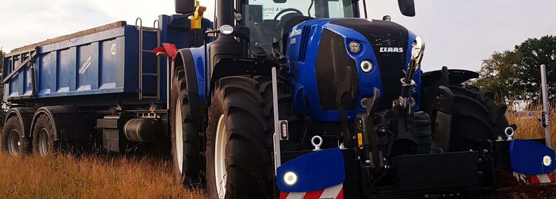 Ein blauer Traktor steht neben einem großen Kipplaster auf einem Feld